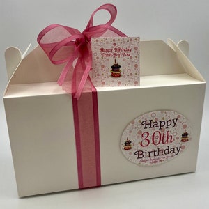 Puede incluir: Caja de regalo blanca con una cinta rosa y una etiqueta rosa y dorada que dice "A Happy Birthday Treat For You". La caja tambi&eacute;n tiene una pegatina rosa y dorada que dice "Happy 30th Birthday Created Especially For You In Trinity Cove"