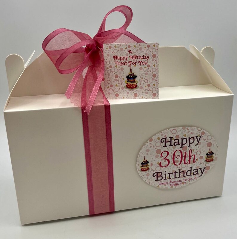 Puede incluir: Caja de regalo blanca con una cinta rosa y una etiqueta rosa y dorada que dice "A Happy Birthday Treat For You". La caja tambi&eacute;n tiene una pegatina rosa y dorada que dice "Happy 30th Birthday Created Especially For You In Trinity Cove"