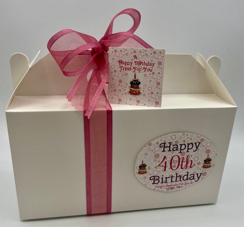 Puede incluir: Una caja de regalo blanca con una cinta rosa y una etiqueta rosa que dice "A Happy Birthday Treat For You". La caja tambi&eacute;n tiene una pegatina rosa y blanca que dice "Happy 40th Birthday Created Especially For You".