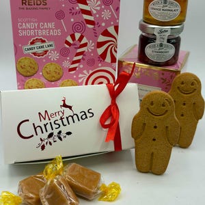 May include: A gift set featuring a pink box of Reids Scottish Candy Cane Shortbreads, two small Tiptree jars of orange marmalade and strawberry preserve, a white Merry Christmas box with a red ribbon, and two gingerbread cookies.