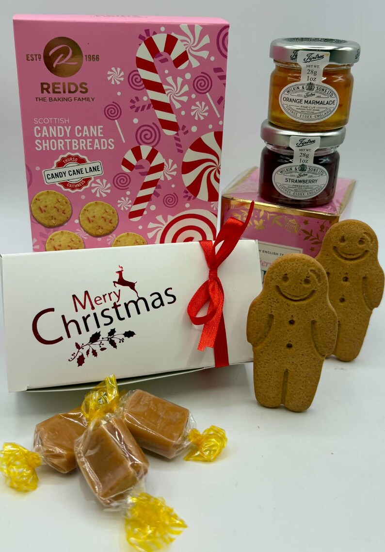 May include: A gift set featuring a pink box of Reids Scottish Candy Cane Shortbreads, two small Tiptree jars of orange marmalade and strawberry preserve, a white Merry Christmas box with a red ribbon, and two gingerbread cookies.