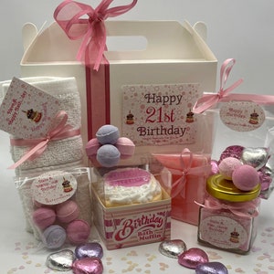 Puede incluir: Una caja de regalo blanca llena de productos de ba&ntilde;o rosas y blancos para un 21 cumplea&ntilde;os. La caja incluye una toalla de ba&ntilde;o, bombas de ba&ntilde;o, sales de ba&ntilde;o, un muffin de ba&ntilde;o y una pastilla de jab&oacute;n. La caja est&aacute; decorada con una cinta rosa y una tarjeta que dice "Feliz 21 cumplea&ntilde;os".