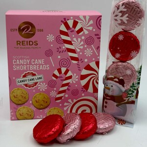 May include: A pink rectangular box of Reids Scottish Candy Cane Shortbreads featuring candy cane and peppermint graphics, alongside a clear vertical sleeve containing four round cookies wrapped in red and pink foil with snowflake patterns.