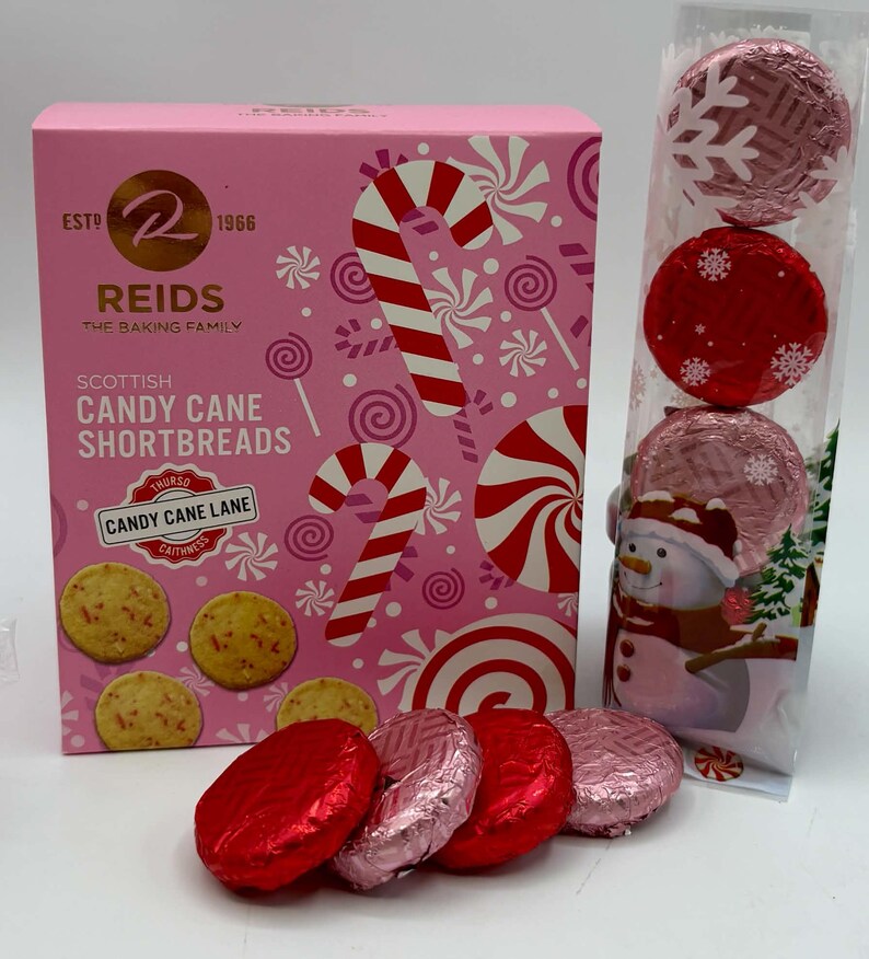 May include: A pink rectangular box of Reids Scottish Candy Cane Shortbreads featuring candy cane and peppermint graphics, alongside a clear vertical sleeve containing four round cookies wrapped in red and pink foil with snowflake patterns.