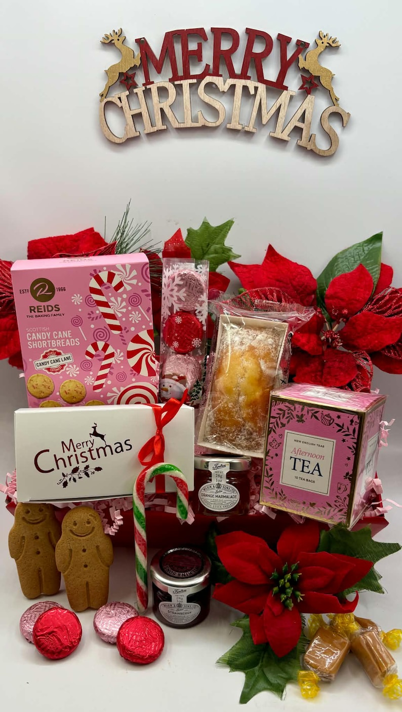 May include: A Christmas gift hamper containing Reids candy cane shortbread, a loaf cake, New English Tea, two jars of jam, gingerbread cookies, foil-wrapped chocolates, and a candy cane, accented with red poinsettia flowers and a Merry Christmas sign.