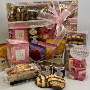 May include: A gift hamper containing various food items including a pink box of Afternoon Tea, a fruit cake, jars of marmalade and strawberry jam, assorted cookies, and a bag of pink and white Luxury Fudge with a decorative pink ribbon.
