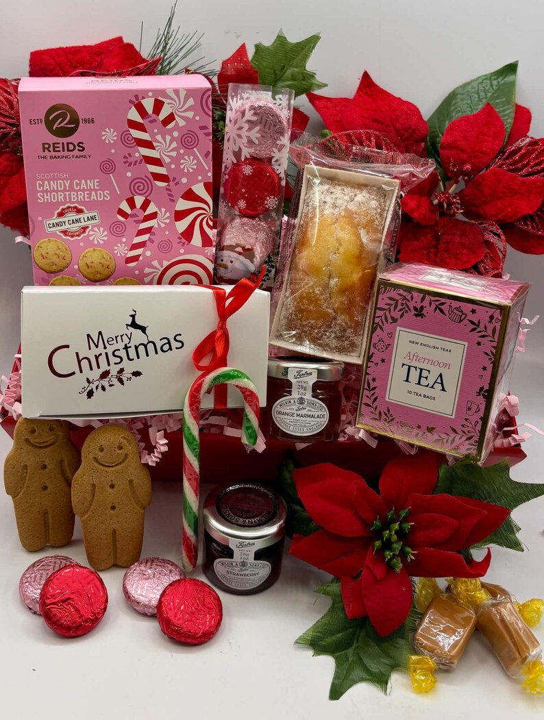 May include: A holiday gift hamper containing Reids Candy Cane Shortbreads, a Merry Christmas box, New English Tea, two gingerbread cookies, two jars of preserves, a candy cane, wrapped chocolates, and red poinsettia floral decorations.