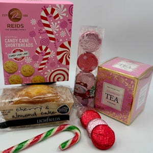 May include: A collection of holiday treats including a pink box of Reids Scottish Candy Cane Shortbreads, a clear tube of red and pink foil-wrapped chocolates, a box of New English Tea Afternoon Tea, and a Lichfields cherry and almond cake.