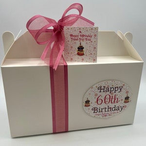 Puede incluir: Una caja de regalo blanca con una cinta rosa y una etiqueta que dice "A Happy Birthday Treat For You". La caja tambi&eacute;n tiene una pegatina que dice "Happy 60th Birthday Created Especially For You With Love".