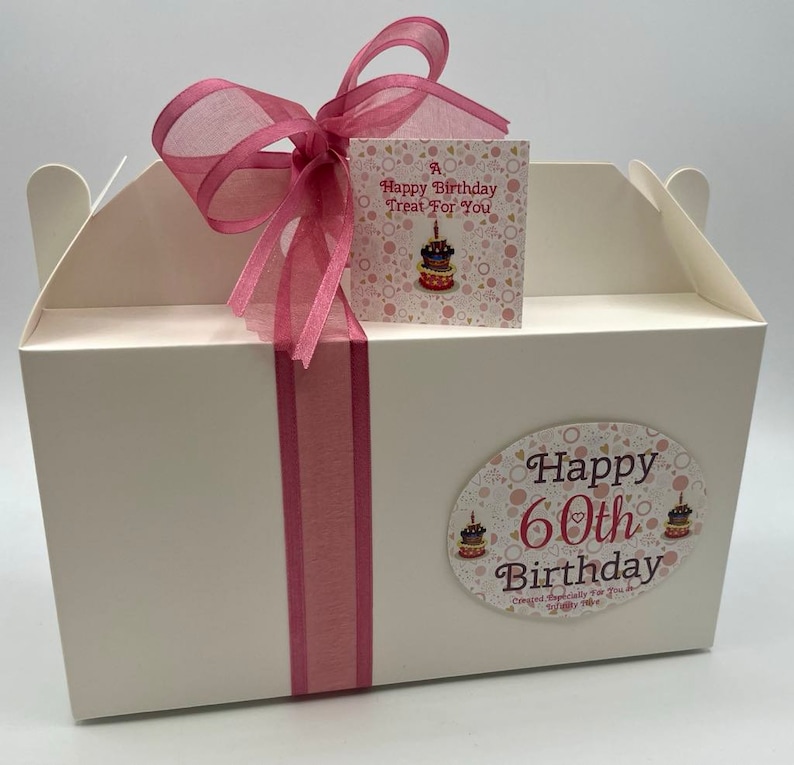 Puede incluir: Una caja de regalo blanca con una cinta rosa y una etiqueta que dice "A Happy Birthday Treat For You". La caja tambi&eacute;n tiene una pegatina que dice "Happy 60th Birthday Created Especially For You With Love".