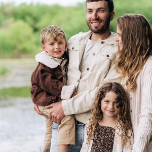 Puede incluir: Una familia de cuatro personas posando junta al aire libre. Un progenitor viste una chaqueta vaquera color crema, el otro un c&aacute;rdigan crema sobre una blusa marr&oacute;n estampada. Un ni&ntilde;o peque&ntilde;o lleva una chaqueta de pana marr&oacute;n con forro de sherpa.