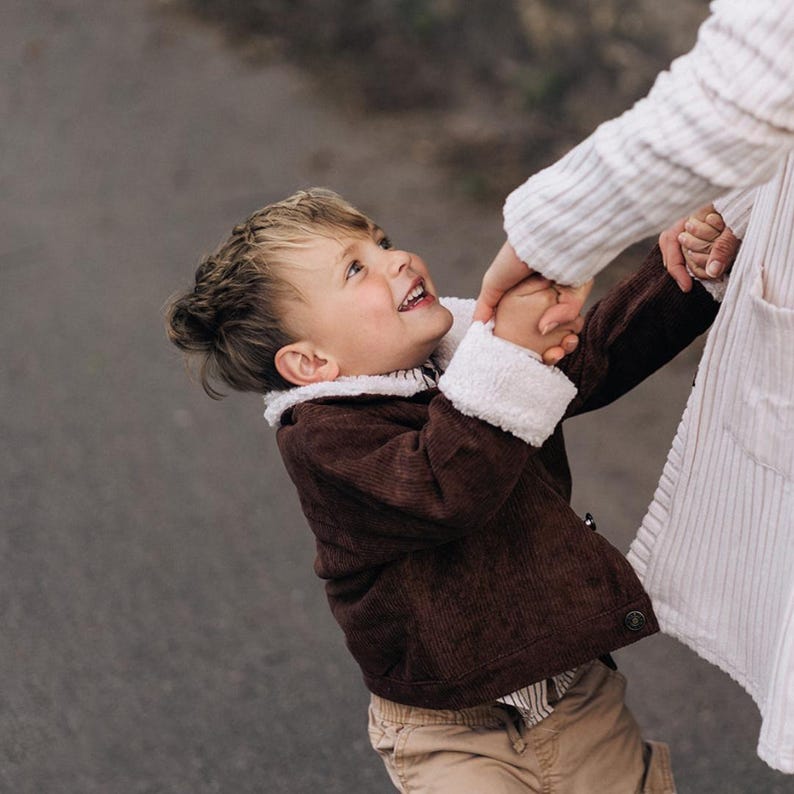 Puede incluir: Un ni&ntilde;o viste una chaqueta de pana marr&oacute;n oscuro con cuello y pu&ntilde;os de forro polar sherpa blanco, combinada con pantalones de color tostado. La chaqueta presenta un cierre frontal de botones y un acabado de tela texturizada muy c&aacute;lido.