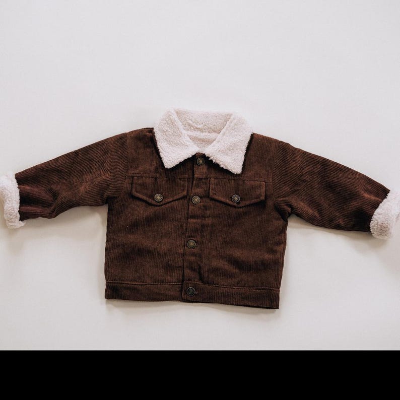 Puede incluir: Una chaqueta de pana marr&oacute;n oscuro con cuello de sherpa blanco y pu&ntilde;os de sherpa a juego. La chaqueta incluye cierre frontal de botones, dos bolsillos en el pecho con solapas abotonadas y mangas largas, ofreciendo un aspecto texturizado.