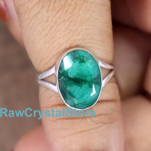 Peut inclure: Une bague en argent avec une émeraude ovale verte. La bague est portée sur un doigt.