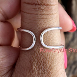 May include: A silver thumb ring with a unique double-loop design. The ring is worn on a person's thumb.