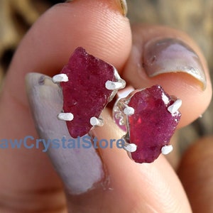 May include: A pair of silver earrings featuring raw ruby gemstones. The rubies are a deep red colour and have a natural, unpolished appearance.