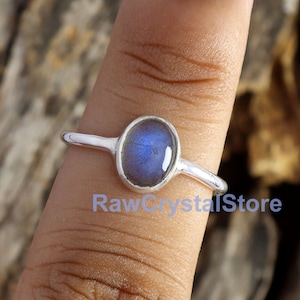 May include: A silver ring with a blue oval labradorite gemstone. The ring is on a finger with green nail polish.