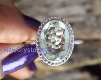 May include: A silver ring with a light green oval gemstone. The ring has a rope-like design around the edge of the setting.