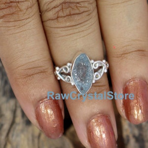 May include: A silver ring featuring a light blue aquamarine gemstone. The ring has a delicate, ornate design.