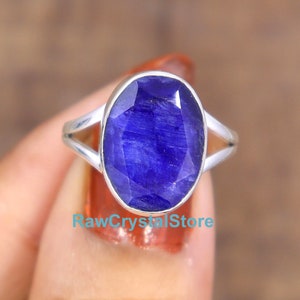 Puede incluir: Un anillo de plata con una gran piedra de zafiro azul ovalada. El anillo tiene un diseño simple con una banda delgada y una banda dividida a cada lado de la piedra.