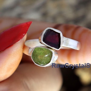 May include: A silver ring with a green and red gemstone. The ring is on a finger with red nail polish. The text "RawCrystalStore" is visible in the image.