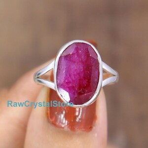 May include: A silver ring with a large oval-shaped ruby gemstone. The ruby is a deep pink color and has a faceted cut.