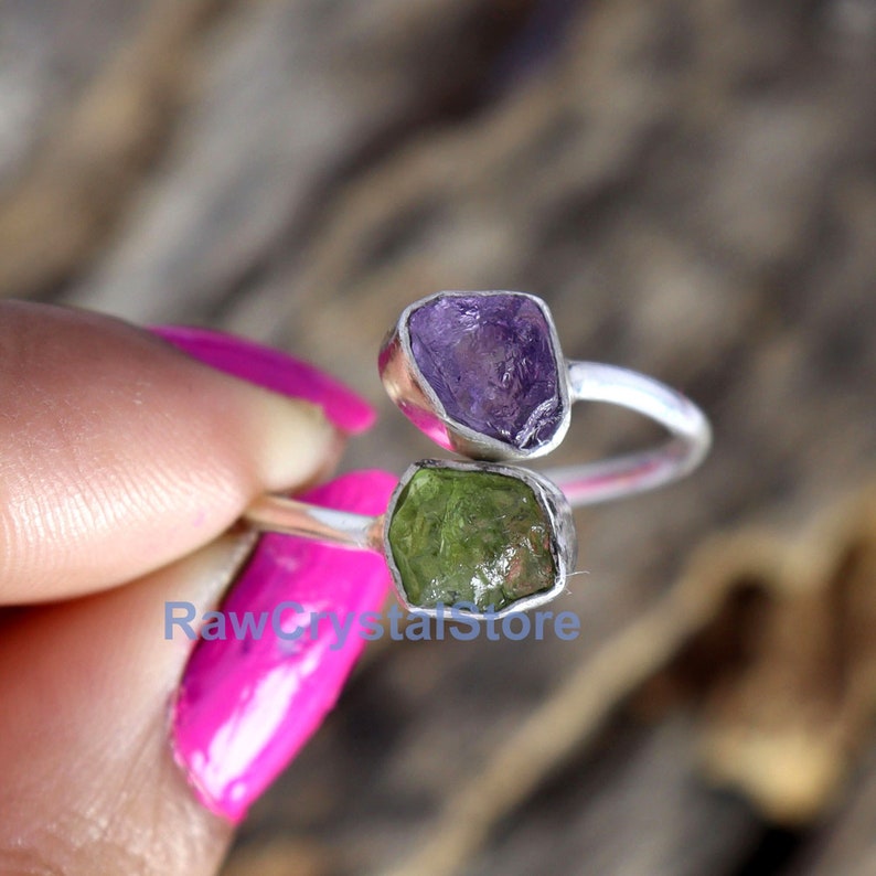 May include: A silver ring with two raw gemstones. The ring is adjustable and features a purple amethyst and a green peridot.