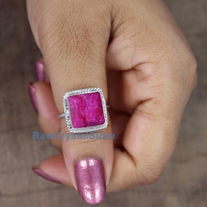 Pode incluir: Um anel de prata com uma pedra preciosa rosa quadrada. O anel &eacute; engastado em uma banda de prata com um design de corda.