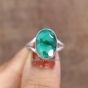 May include: A silver ring with a large, oval-shaped emerald gemstone. The emerald is a deep green color and has a faceted cut.