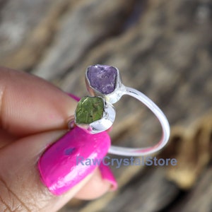 May include: A silver ring with two raw gemstones. The ring has a purple amethyst and a green peridot.