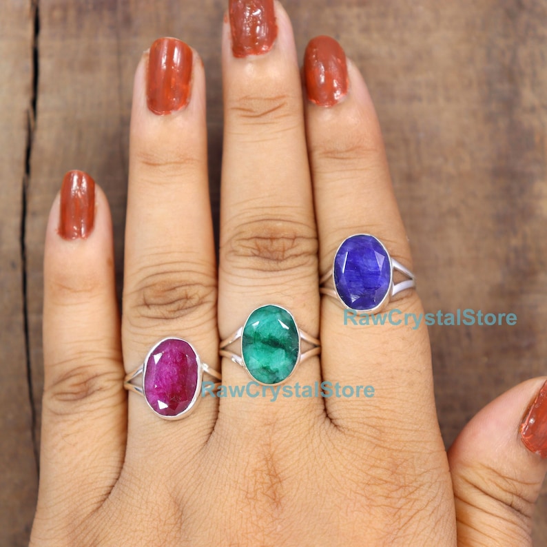 May include: Four silver rings with oval-shaped gemstones. The rings feature a split shank design. The gemstones are red, green, blue, and purple.