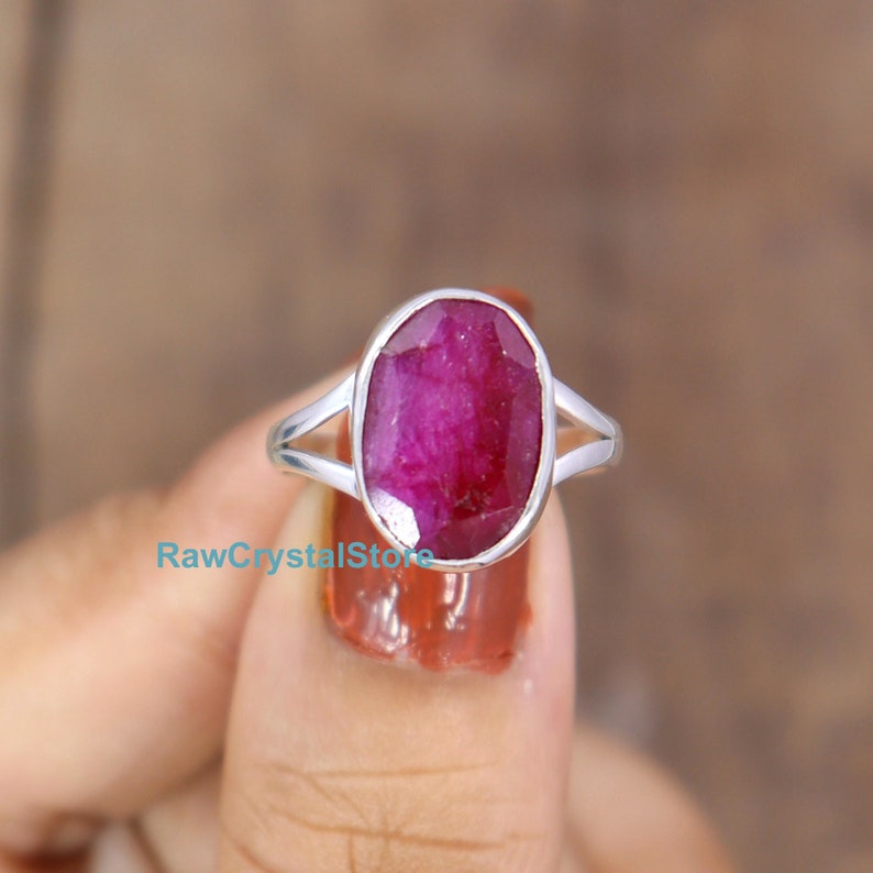 May include: A silver ring with a large oval-shaped ruby gemstone. The ruby is a deep pink color and has a faceted cut.