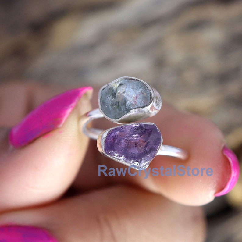 May include: A silver ring with a light blue aquamarine and a purple amethyst stone. The ring is adjustable and can be worn on any finger.