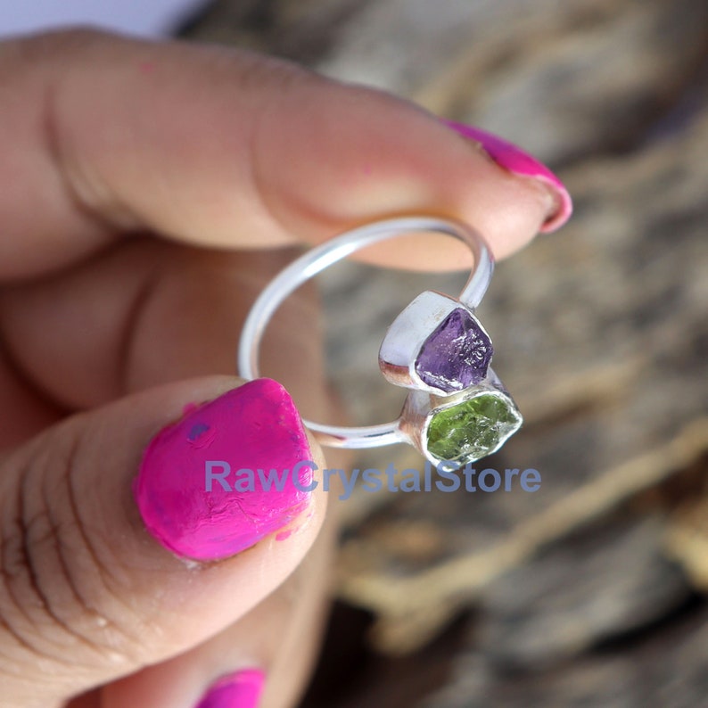 May include: A silver ring with a purple amethyst and a green peridot stone. The ring is set in a simple band and the stones are raw and uncut.