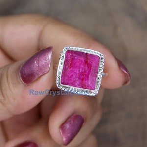 Pode incluir: Um anel de prata com uma gema de rubi rosa quadrada engastada em uma banda de prata torcida.