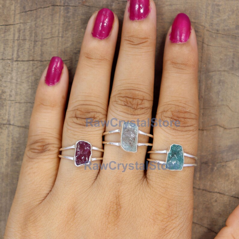 Peut inclure: Trois bagues en argent avec des pierres brutes. Les pierres sont rectangulaires et de couleurs rouge, bleu clair et turquoise. Les bagues sont pr&eacute;sent&eacute;es sur une main avec du vernis &agrave; ongles rose.