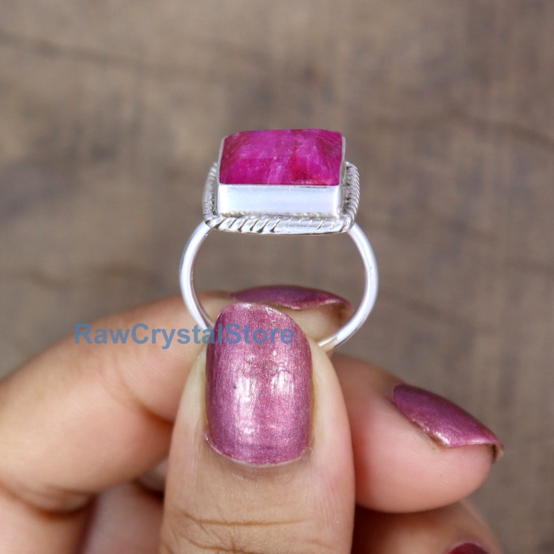 Pode incluir: Um anel de prata com uma gema de rubi quadrada e facetada. O anel tem uma banda tran&ccedil;ada.