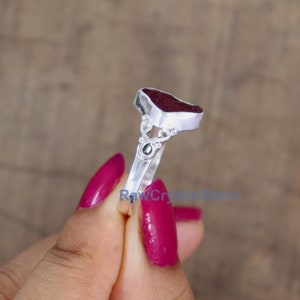 May include: A silver ring featuring a heart-shaped ruby gemstone. The ring has a delicate design with a small black stone accent.