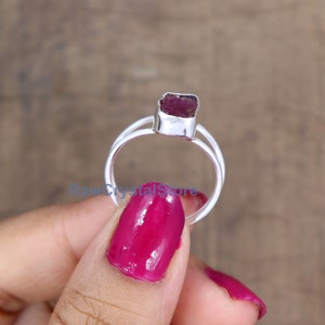 Peut inclure: Bague en argent orn&eacute;e d'une pierre brute rouge fonc&eacute;. La bague pr&eacute;sente un design &agrave; tige fendue, avec deux bandes se rejoignant. La pierre est rectangulaire et sertie dans une lunette en argent.