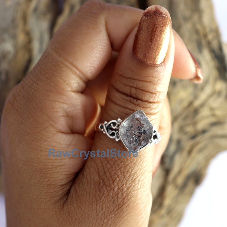 May include: A silver ring featuring a clear, faceted, square-shaped gemstone. The ring has a delicate, ornate design.