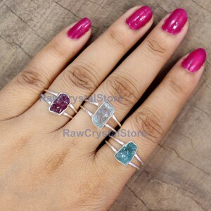 Peut inclure: Trois bagues en argent, chacune orn&eacute;e d'une pierre brute rectangulaire de couleur rouge, bleu clair et turquoise. Les bagues ont un design &agrave; double anneau. L'image est sur un fond neutre.