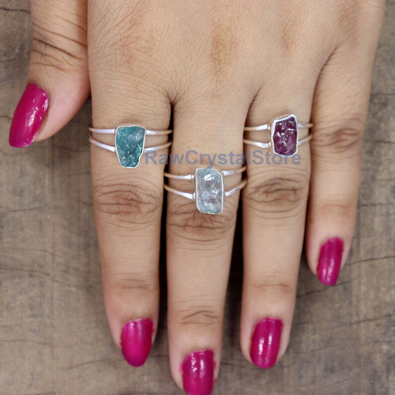 Peut inclure: Trois bagues en argent, chacune orn&eacute;e d'une pierre brute rectangulaire. Les pierres sont de couleur teal, bleu clair et magenta. Les bagues sont pr&eacute;sent&eacute;es sur une main avec des ongles vernis magenta.
