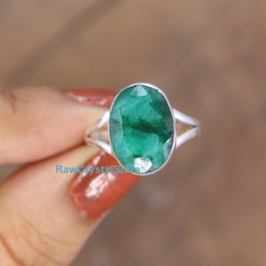 May include: A silver ring with a large, oval-shaped emerald gemstone. The emerald is a deep green color and has a faceted cut.