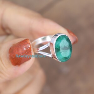 May include: A silver ring with a large, oval-shaped emerald green gemstone. The ring is set in a simple, elegant design.