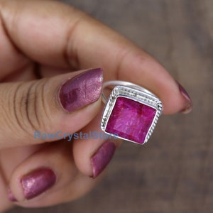 Pode incluir: Um anel de prata com uma gema de rubi de forma quadrada. O rubi &eacute; de cor rosa intenso e tem um corte facetado. O anel tem um design simples e elegante.