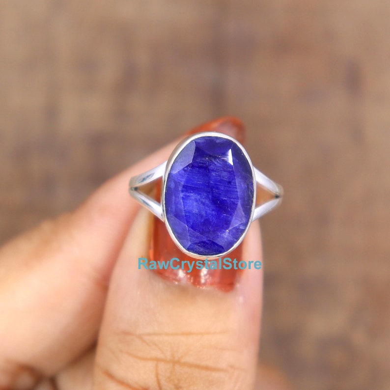 May include: A sterling silver ring with a deep blue oval sapphire gemstone. The ring has a simple, elegant design with a split shank.
