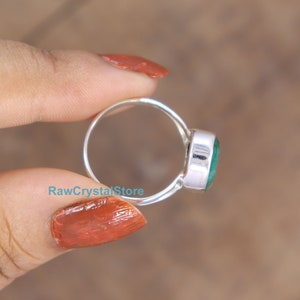 May include: A silver ring with a green oval gemstone. The ring is on a finger.