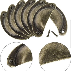 May include: Set of six antique brass cabinet knobs with a rounded, half-circle shape. The knobs have a distressed finish and come with screws.