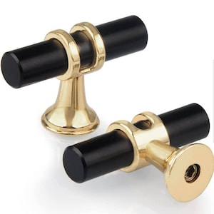 May include: Two black and gold cabinet knobs with a T-shaped design. The knobs have a black cylindrical base and a gold base with a ring around the cylinder.