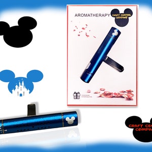 May include: Blue car air freshener with a Mickey Mouse head design. The air freshener is made of metal and has a clip on the back to attach to a vent. The packaging shows a blue air freshener with rose petals scattered around it. The text on the packaging reads "Aromatherapy" and "Craft Central Company".